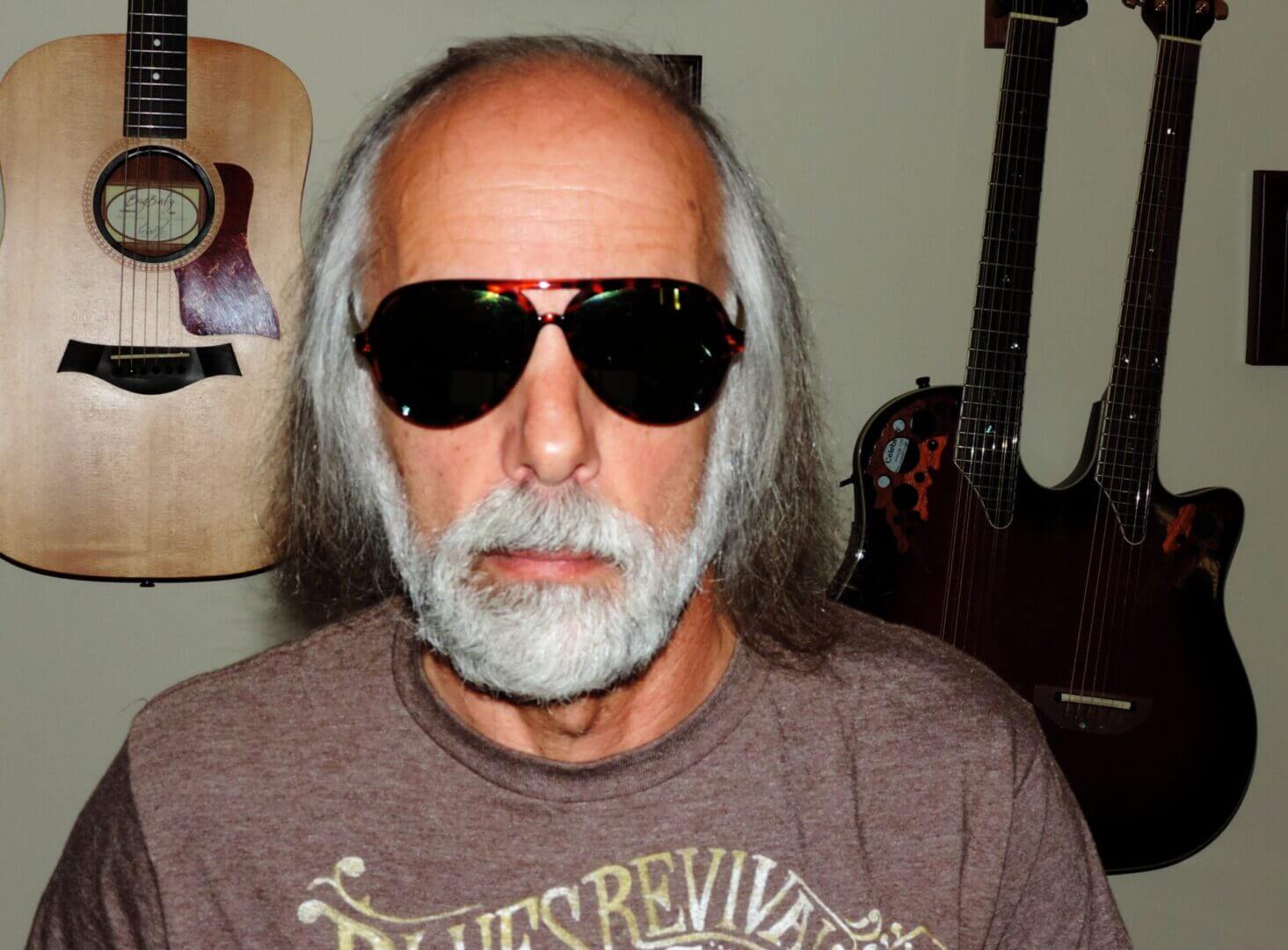 A man with gray hair and beard wearing sunglasses indoors.